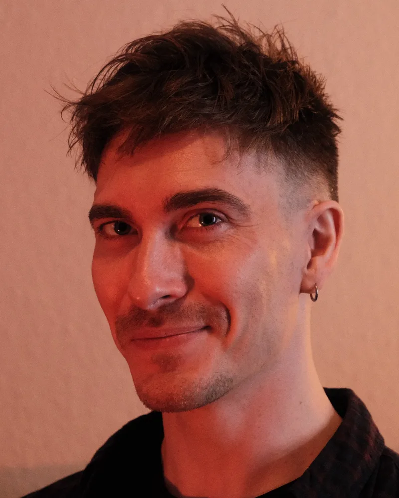 Kevin lächelt schräg in die Kamera, warmes Licht vor heller Wand