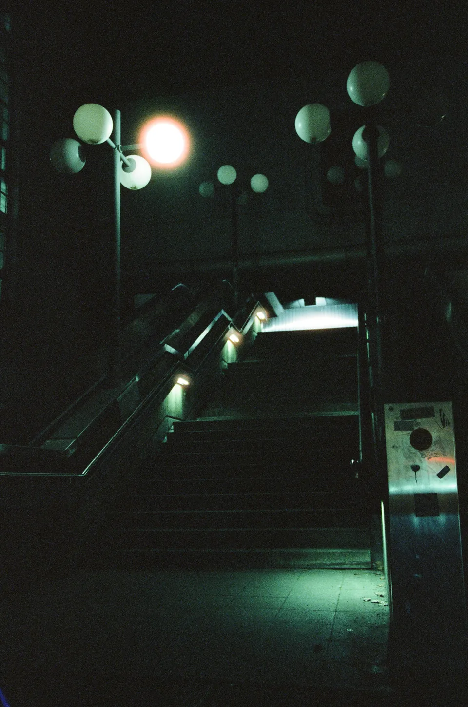 Eine beleuchtete Treppe in einer nächtlichen städtischen Umgebung mit runden Kugelleuchten.