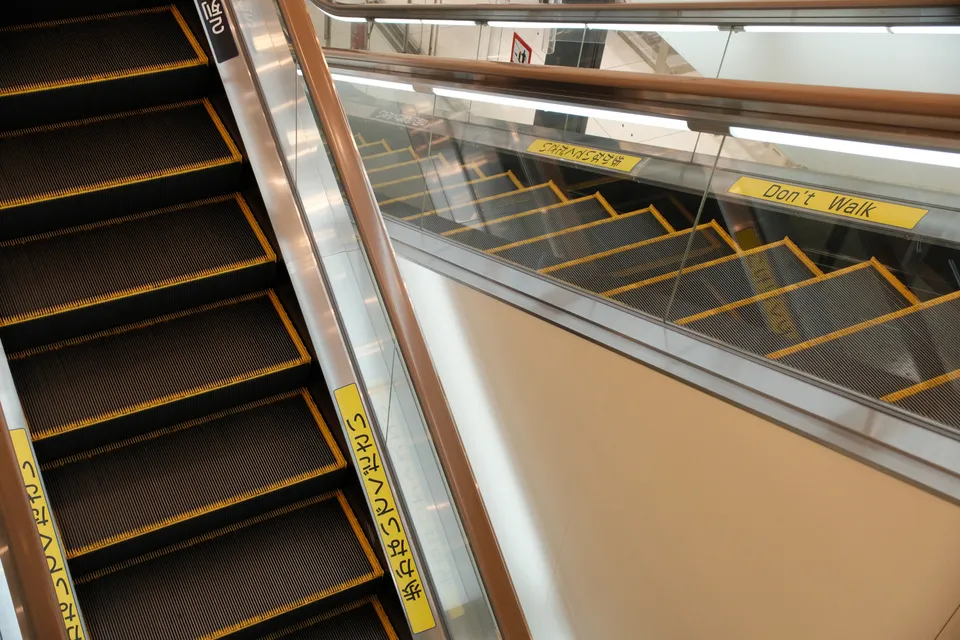 Eine Nahaufnahme von Rolltreppen und Treppenstufen mit gelben Markierungen in einem modernen Gebäude.
