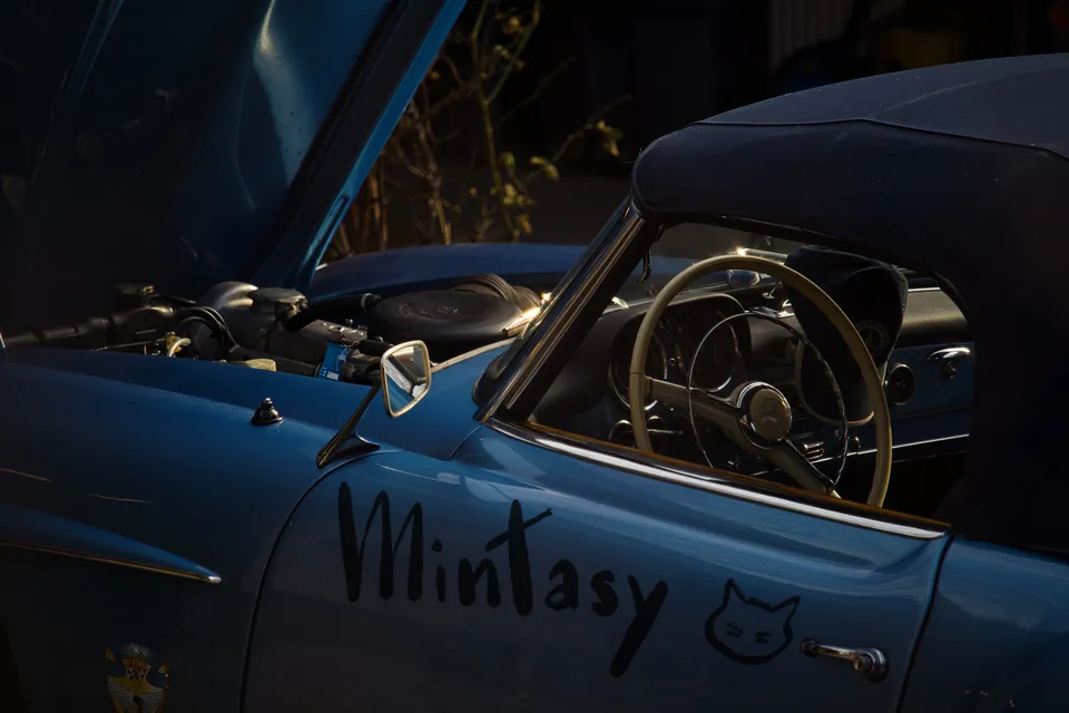 Nahaufnahme eines blauen Oldtimers mit geöffneter Motorhaube und Schriftzug an der Seite.