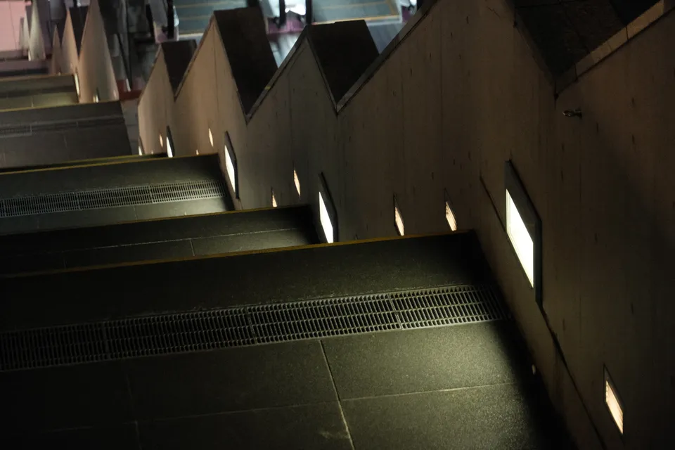 Eine dunkle Treppe mit geometrischen Wänden und eingelassenen Lichtquellen.