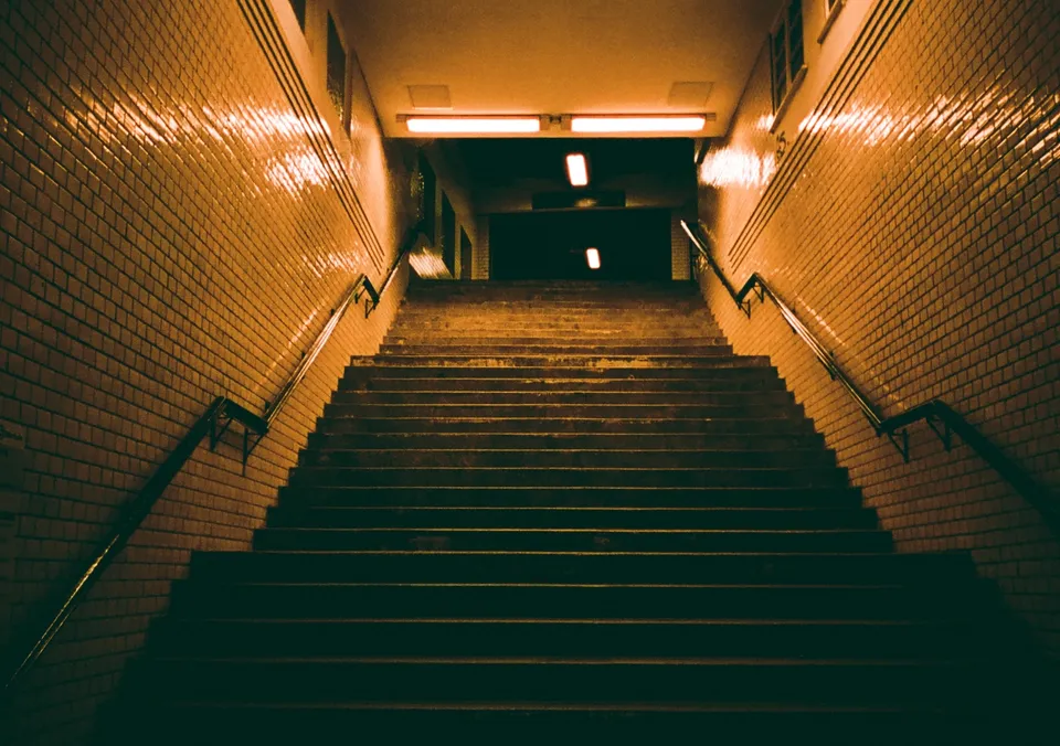 Eine lange Treppe führt in einen beleuchteten Tunnel mit gefliesten Wänden.