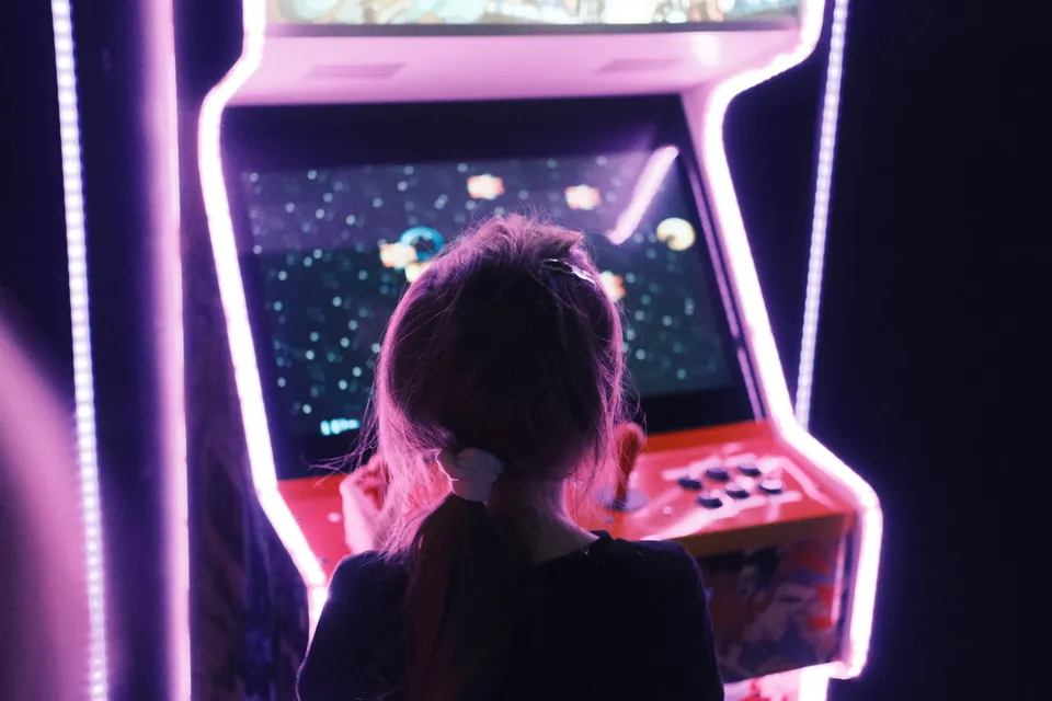 Eine Person betrachtet einen leuchtenden Spielautomaten in einer dunklen Umgebung.