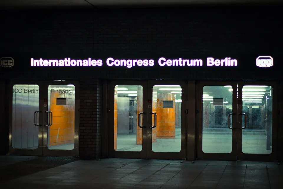 Eine beleuchtete Glasfront mit drei Doppeltüren führt in ein hell erleuchtetes Gebäude bei Nacht.