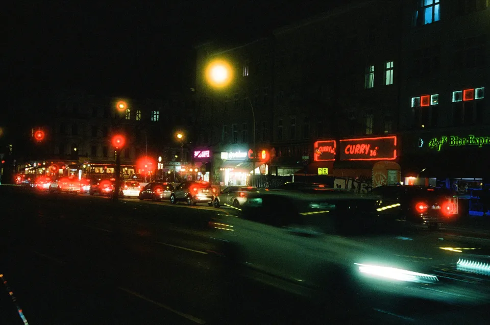 Eine nächtliche Straßenszene mit hell beleuchteten Gebäuden und vielen Autos, deren Rücklichter leuchten.