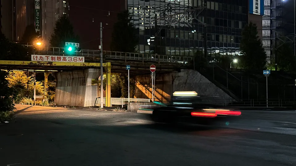 Ein Auto fährt nachts unter einer Überführung in einer beleuchteten Stadt vorbe.