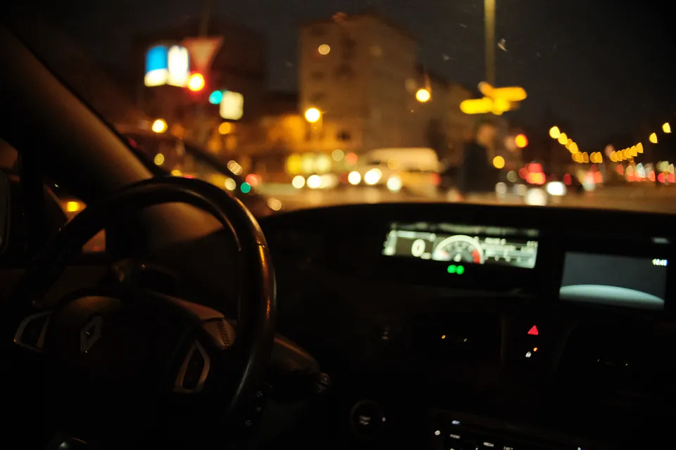 Blick aus dem Cockpit eines Autos auf eine beleuchtete Stadt bei Nacht.
