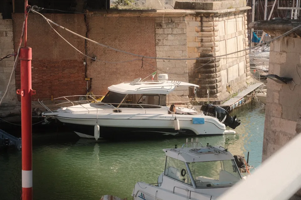 Zwei weiße Motorboote liegen in einem Kanal vor einer historischen Steinmauer.