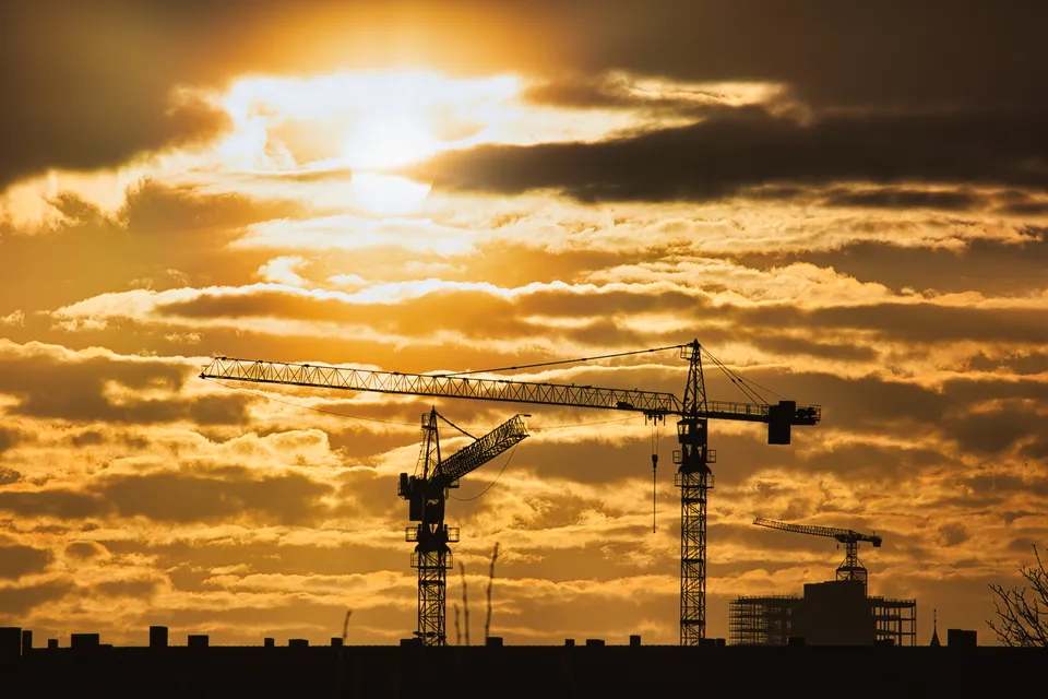 Silhouette von Baukränen vor einem goldenen Wolkenhimmel bei Sonnenuntergang.