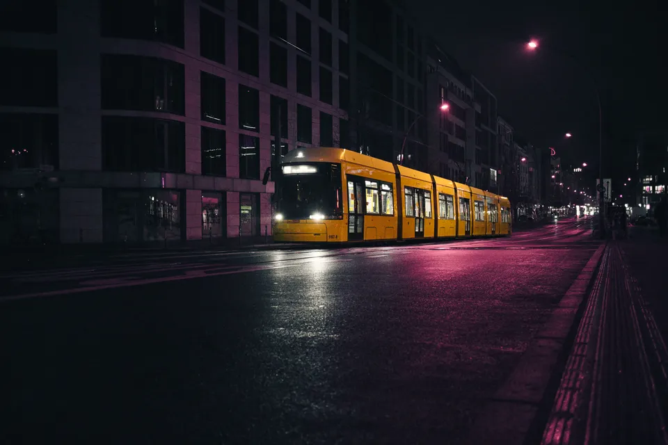 Eine gelbe Straßenbahn fährt nachts durch eine Stadtstraße an beleuchteten Gebäuden vorbei.
