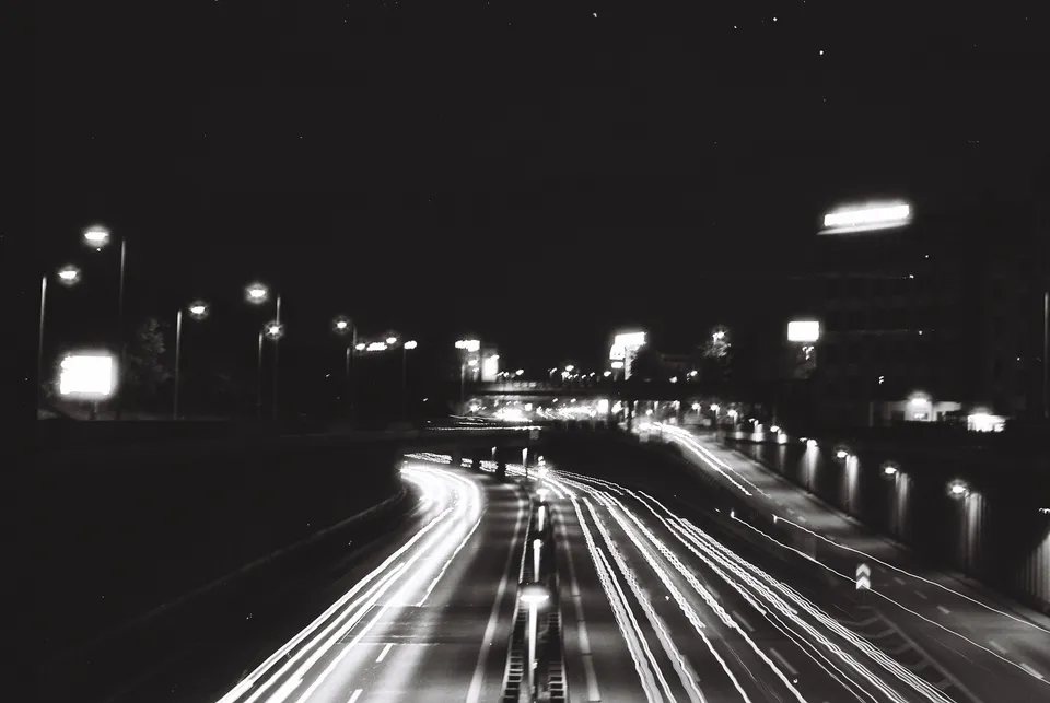 Eine Schwarz-Weiß-Aufnahme mit Langzeitbelichtung zeigt helle Lichtspuren auf einer nächtlichen Autobahn.