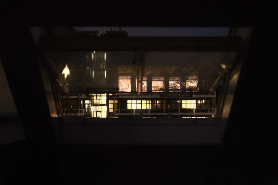 Ein Blick durch ein dunkles Fenster auf beleuchtete Gebäude in der Nacht.
