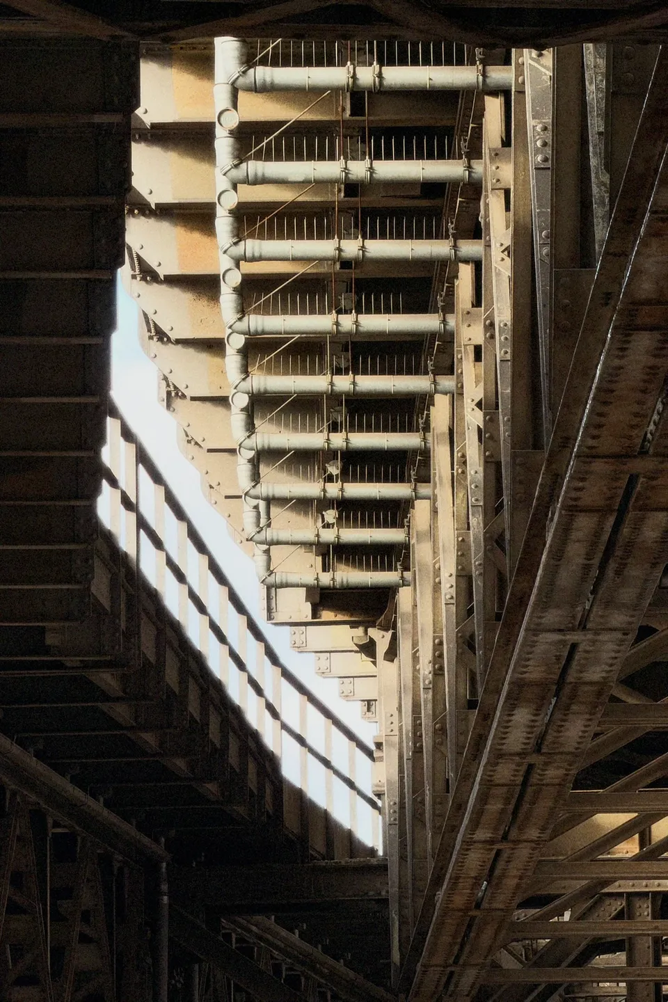 Eine Nahaufnahme der komplexen Stahlkonstruktion und Rohrleitungen einer Brücke aus der Untersicht.