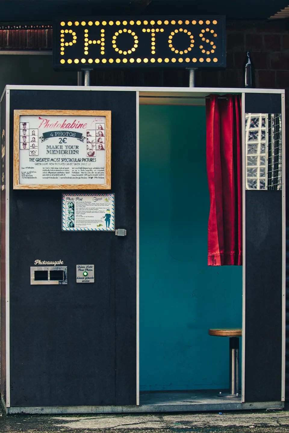 Eine dunkle Fotokabine mit einem leuchtenden Schild, einem roten Vorhang und einem blauen Innenraum.