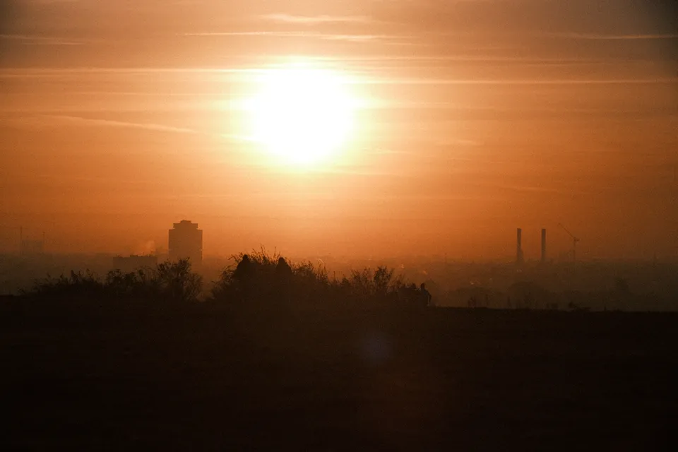 Eine tiefstehende Sonne strahlt über der Silhouette einer Stadt bei nebligem Wetter.
