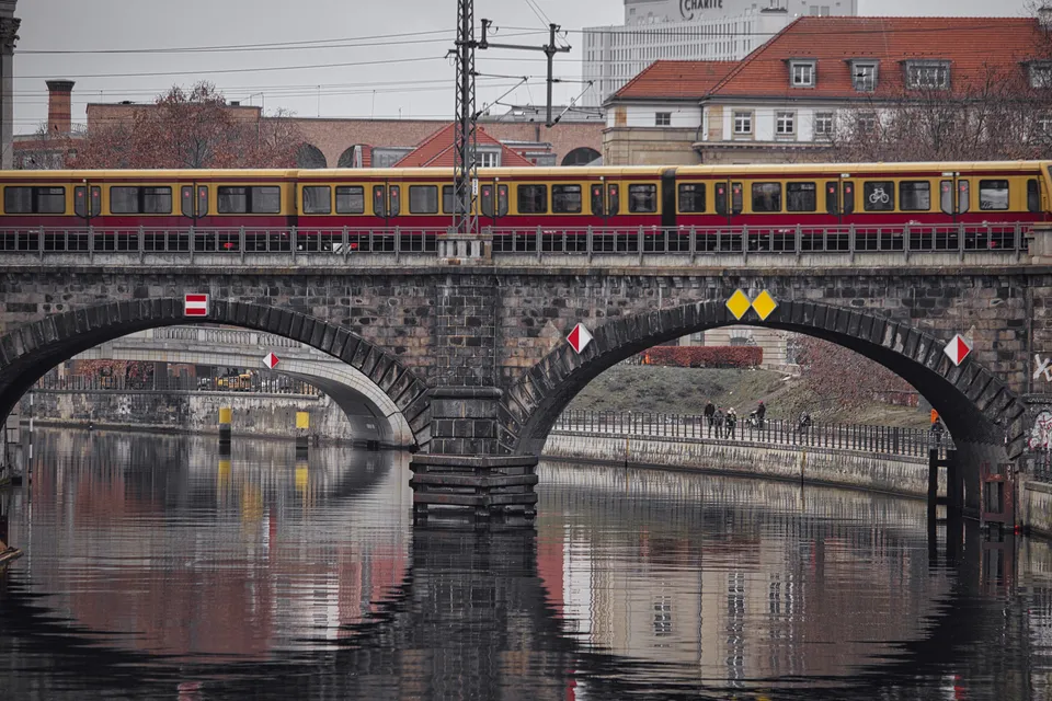 Ein gelb-roter Zug fährt über eine historische Steinbrücke über einen Fluss.