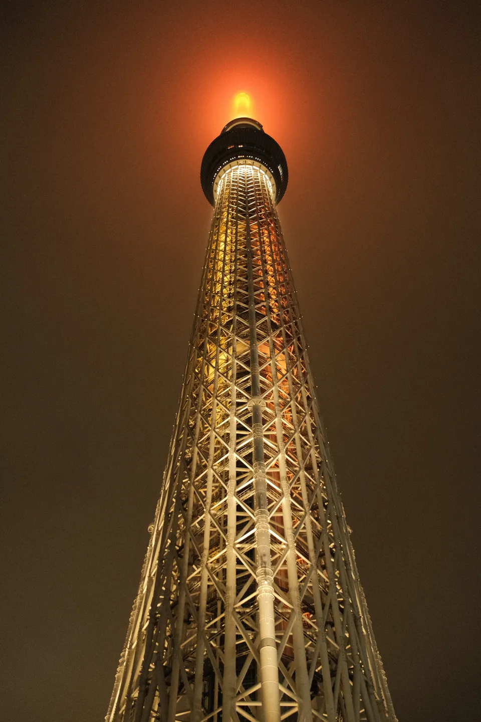 Eine Froschperspektive auf einen hell erleuchteten, gitterartigen Turm bei Nacht.