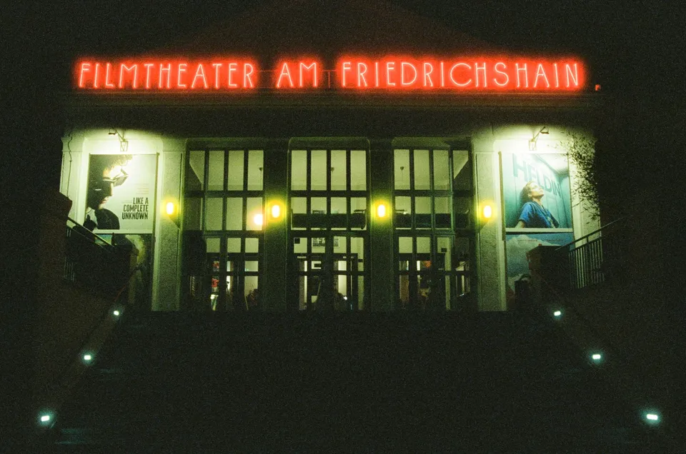 Die beleuchtete Fassade eines Kinos mit leuchtender Beschriftung und Plakaten bei Nacht.