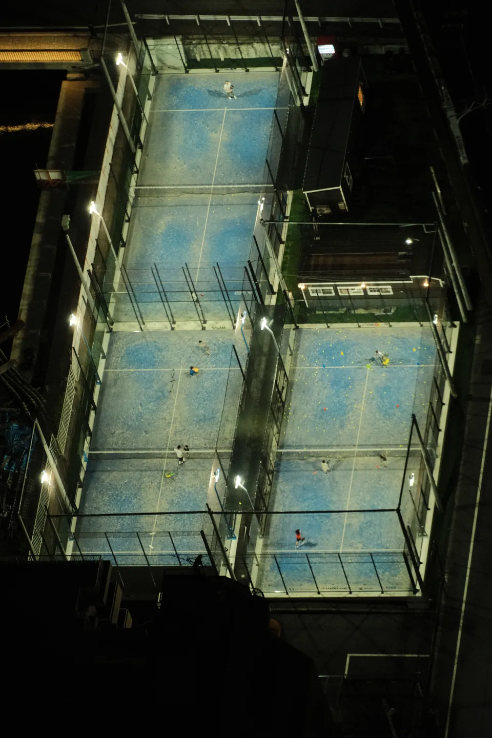 Draufsicht auf beleuchtete blaue Sportplätze bei Nacht mit mehreren Personen.