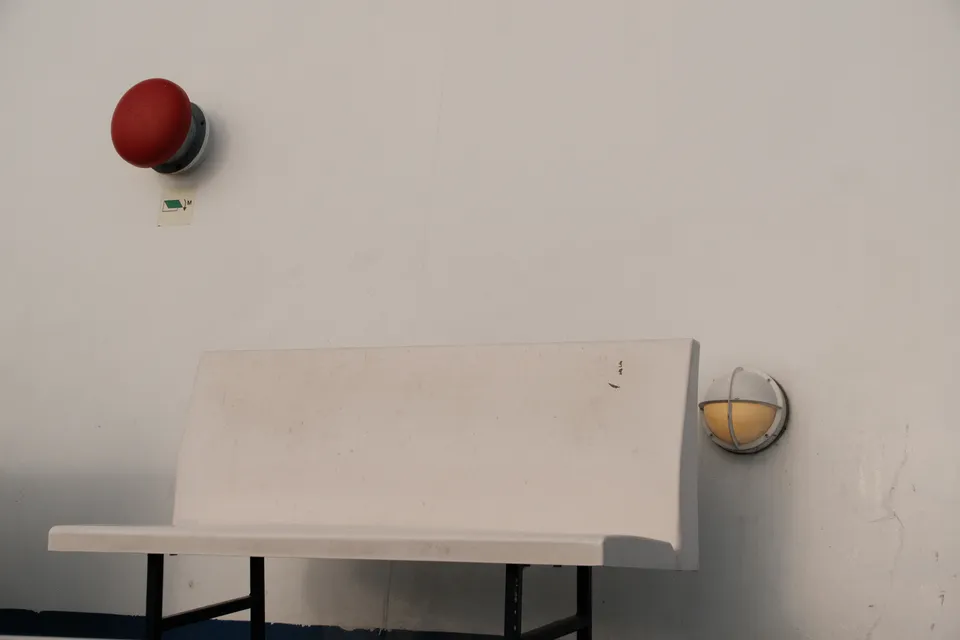 Eine weiße Bank steht vor einer hellen Wand mit zwei runden Wandleuchten.