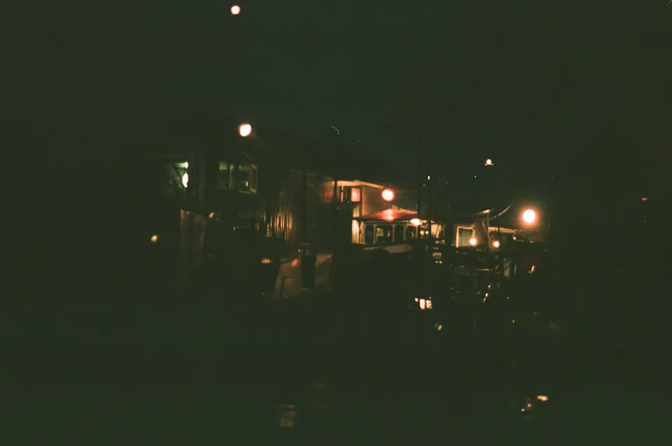 Ein nächtliches Stadtbild mit beleuchteten Gebäuden und Straßenlampen in einer körnigen Analofilm-Ästhetik.