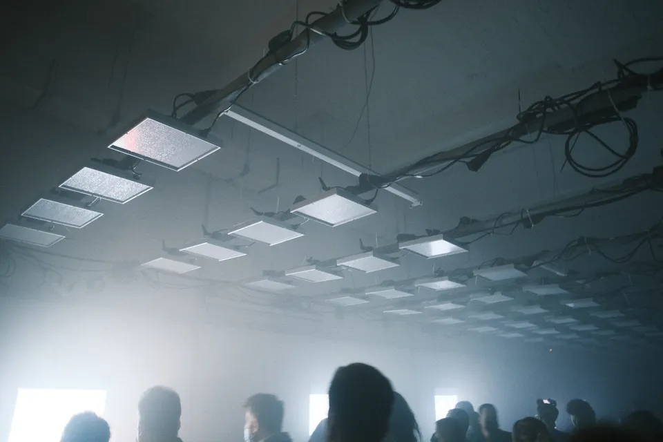 Ein Innenraum mit vielen quadratischen Deckenleuchten und Personen in dichtem Nebel.