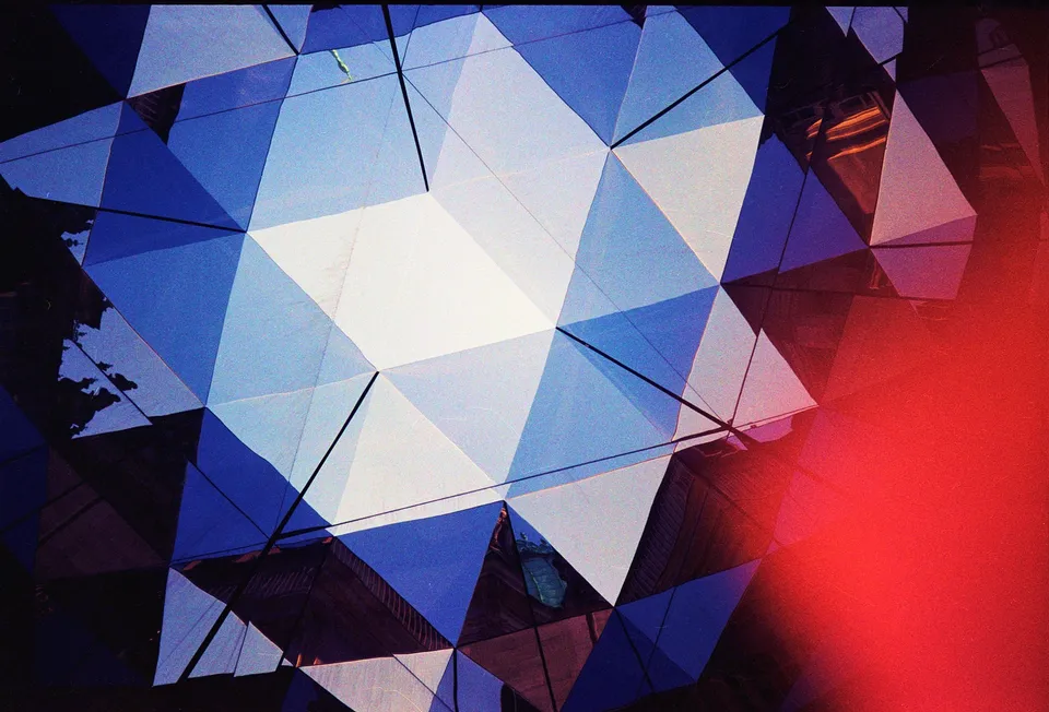 Eine abstrakte Nahaufnahme einer Fassade aus blauen und weißen Dreiecken mit einem roten Lichteffekt.