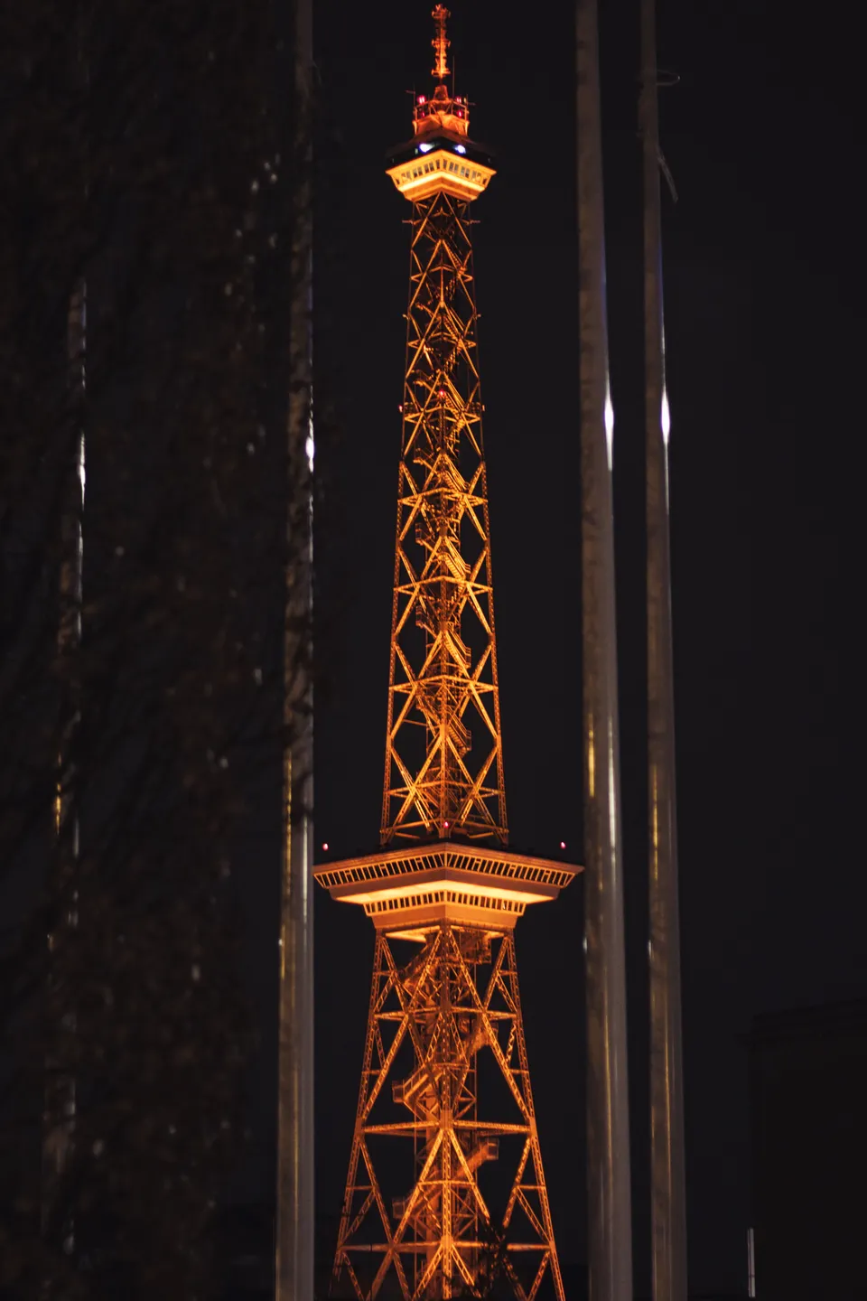 Ein beleuchteter Gittermastturm steht vor dunklen Strukturen bei Nacht.