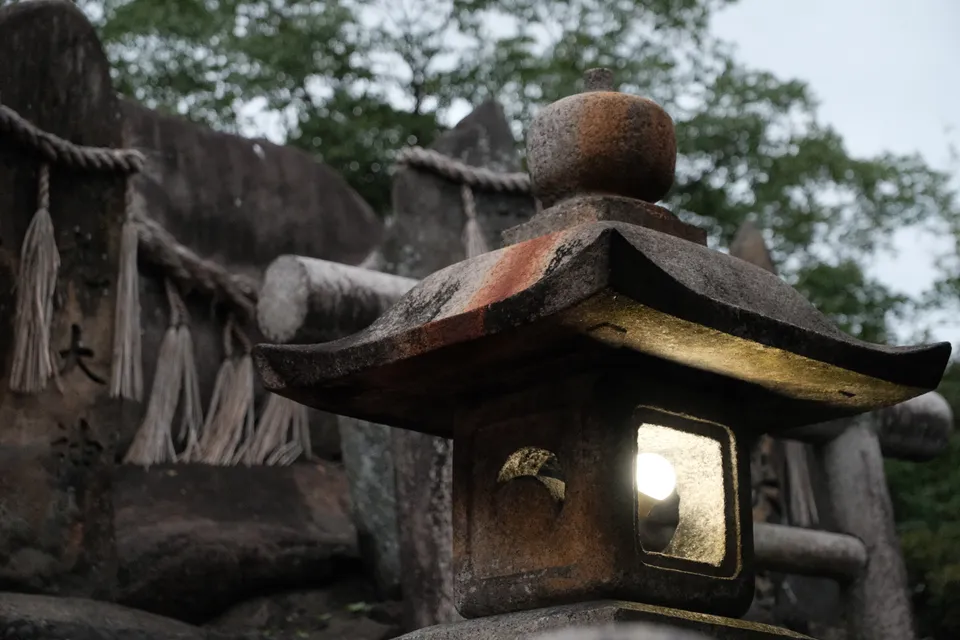 Eine leuchtende Steinstreite vor einem Torii-Tor und einem mit Seilen geschmückten Felsen.