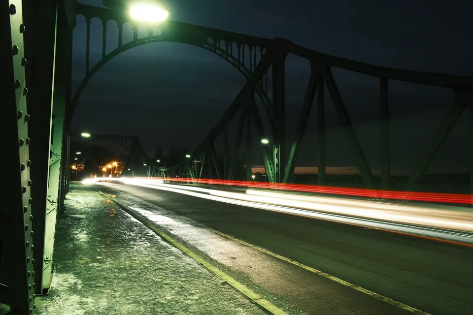 Langzeitbelichtung einer Brücke bei Nacht mit weißen und roten Lichtspuren von Fahrzeugen.