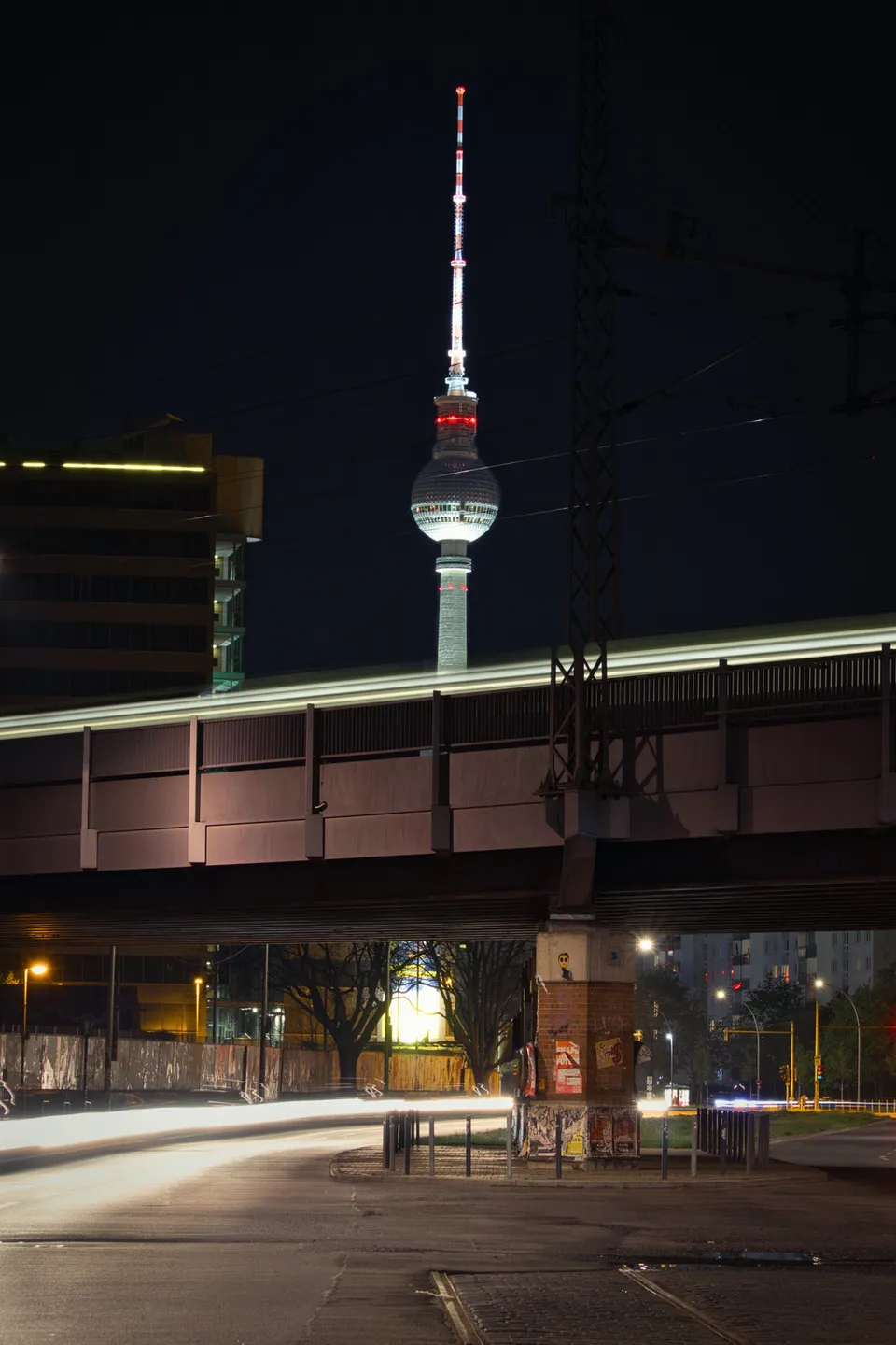 Ein beleuchteter Turm ragt hinter einer Eisenbahnbrücke in den Nachthimmel.