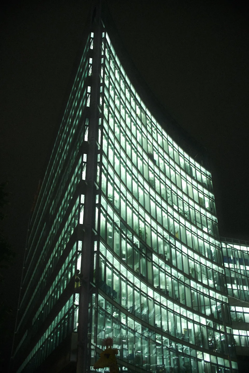 Ein beleuchtetes Bürogebäude mit geschwungener Glasfassade in der Dunkelheit.