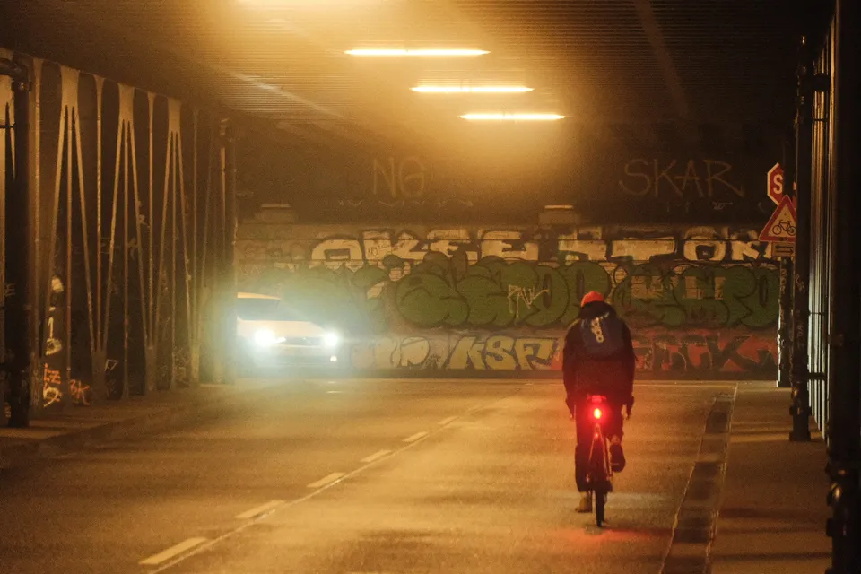Ein Motorradfahrer fährt durch eine beleuchtete Unterführung mit Graffiti-Wänden bei Nacht.