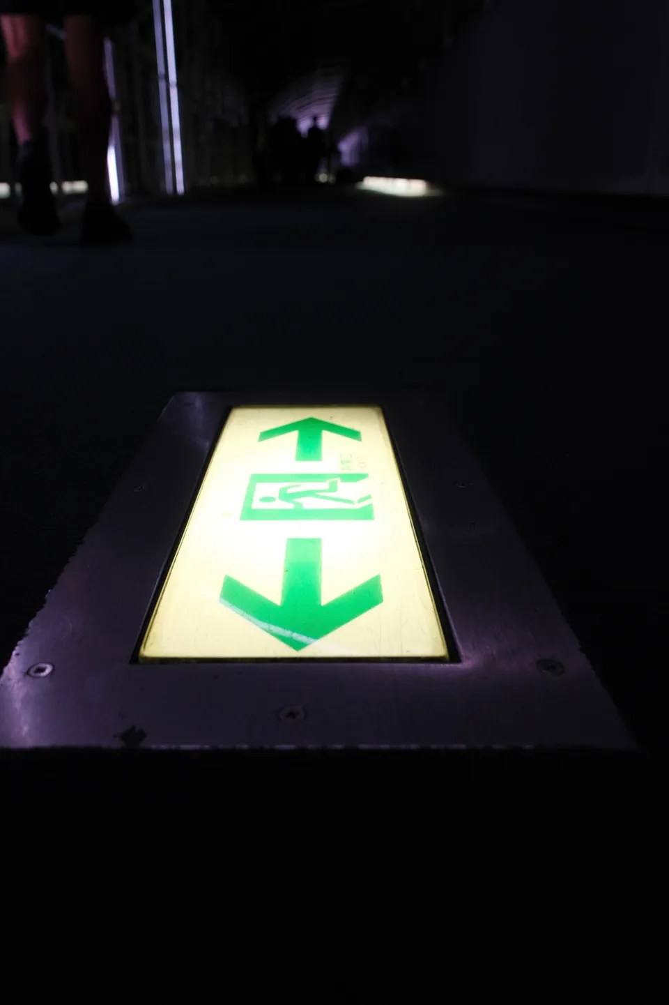 Eine beleuchtete gelbe Bodenplatte mit grünen Pfeilen und einem Symbol in einem dunklen Tunnel.