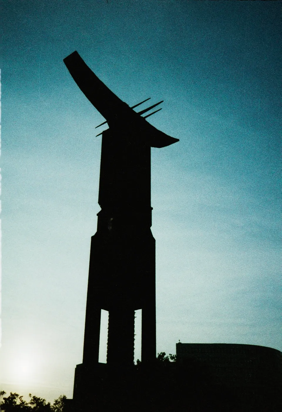 Eine Silhouette eines modernen Turms mit geschwungenem Dach vor einem hellen Himmel.