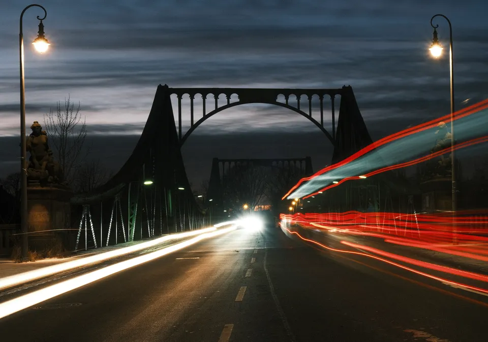 Eine nächtliche Brücke mit langen Lichtspuren von Fahrzeugen und leuchtenden Straßenlaternen.