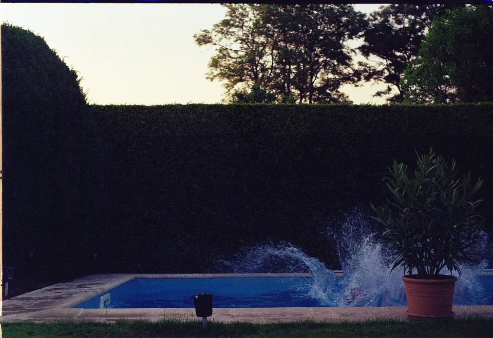 Ein kleiner Pool mit einer aufspritzenden Wasserfontäne vor einer hohen Hecke.