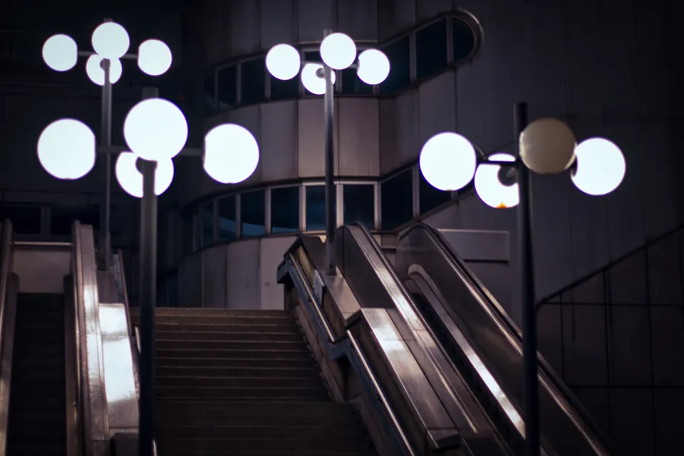 Eine nächtliche Szene mit Rolltreppen und dekorativen weißen Kugelleuchten in einer modernen Architektur.