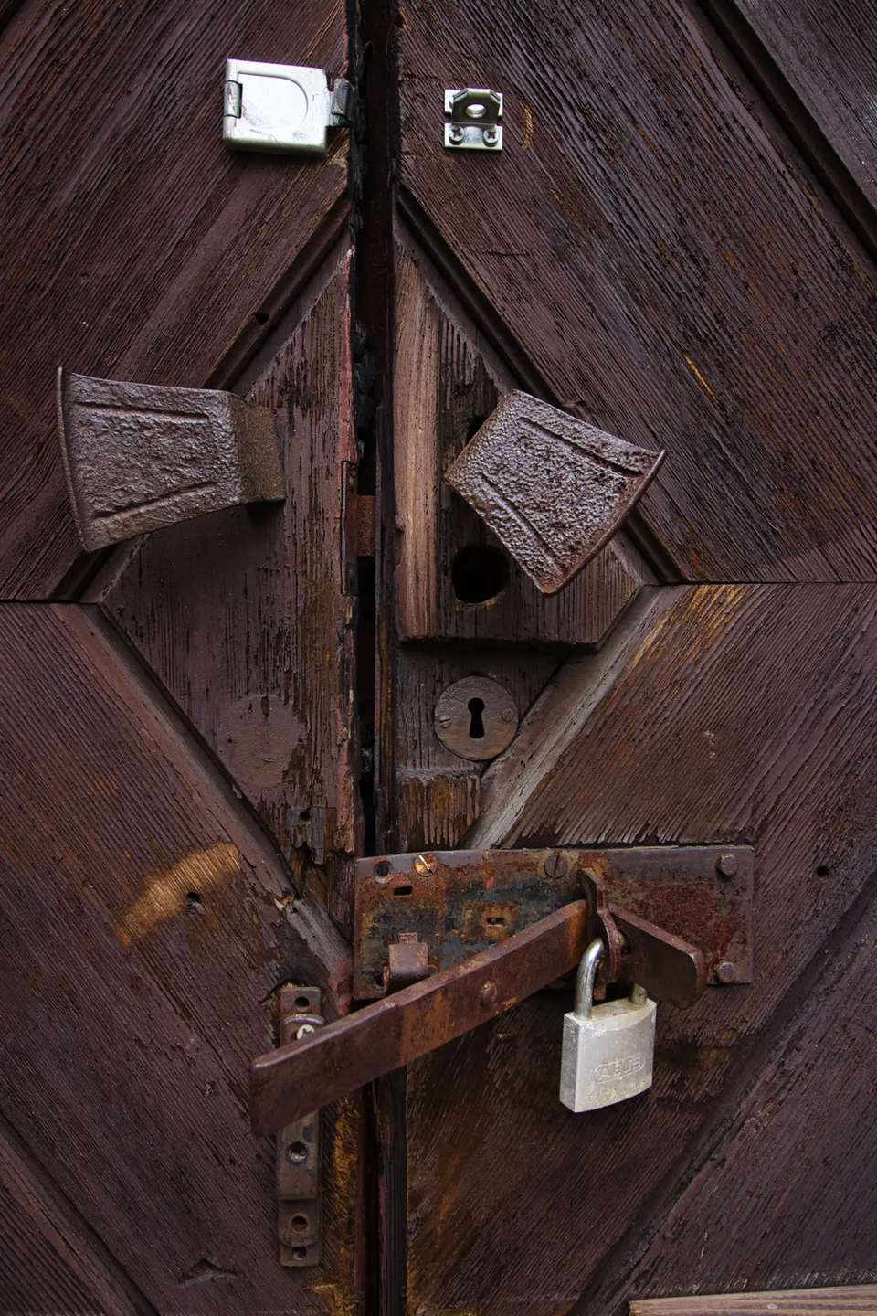 Eine alte, dunkle Holztür mit verschiedenen Schlössern, Riegeln und Metallbeschlägen.