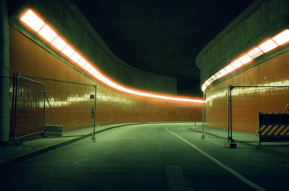 Ein geschwungener Tunnel mit leuchtenden orangefarbenen Lichtbändern und Absperrgittern.