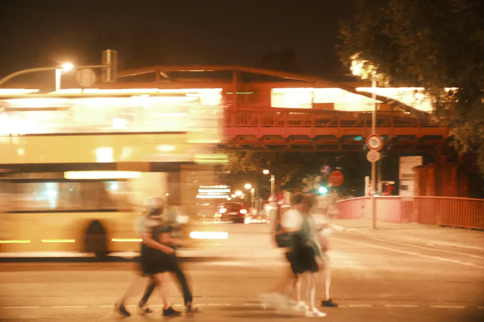 Ein verschwommener Bus fährt nachts an Fußgängern in einer beleuchteten Stadt vorbei.
