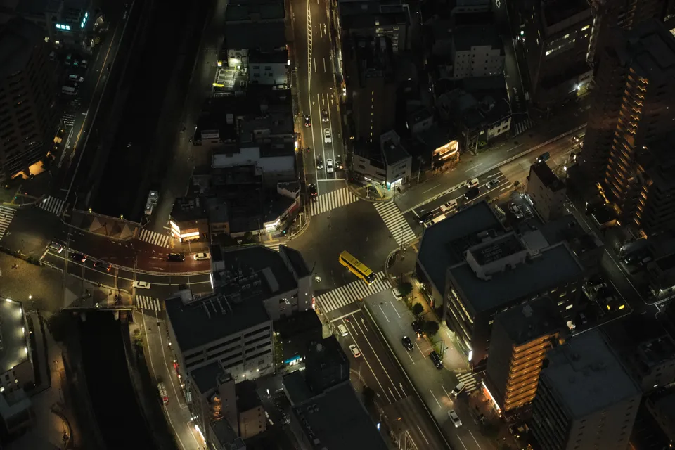 Eine Luftaufnahme einer beleuchteten Stadtkreuzung bei Nacht mit Autos und Gebäuden.