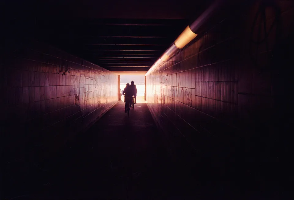 Zwei Personen auf Fahrrädern fahren durch einen langen, hell erleuchteten Tunnel.