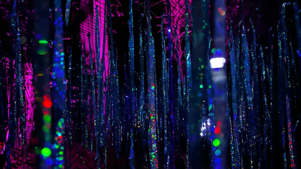 Eine nächtliche Szene mit herabhängenden glitzernden Strängen und bunten Lichtreflexionen.