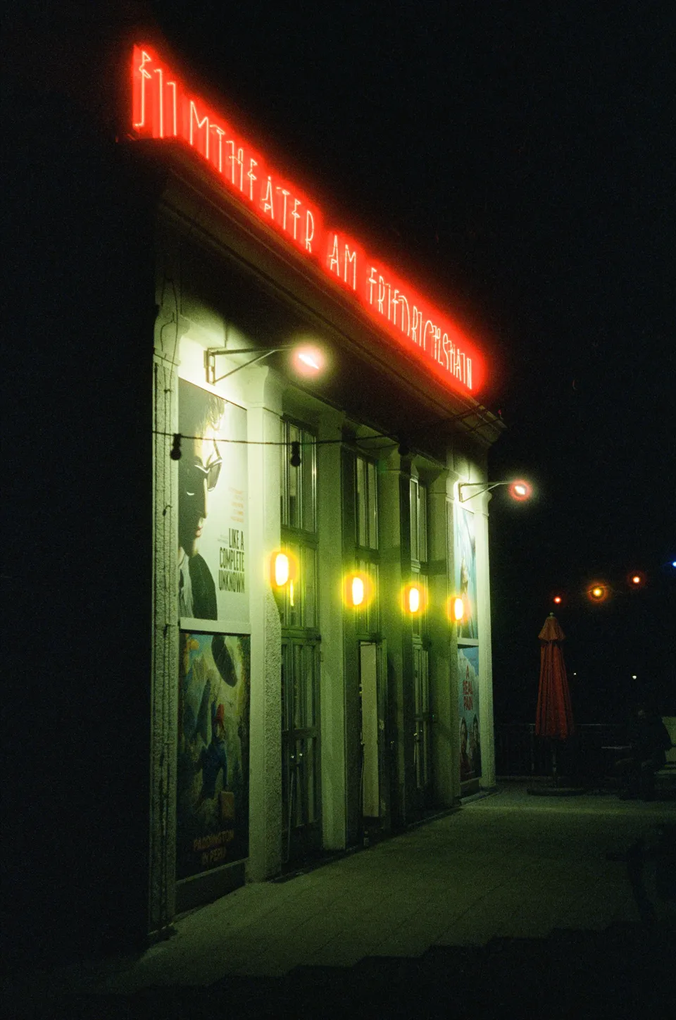 Die Außenansicht eines beleuchteten Kinos mit roten Neonbuchstaben und Plakaten bei Nacht.