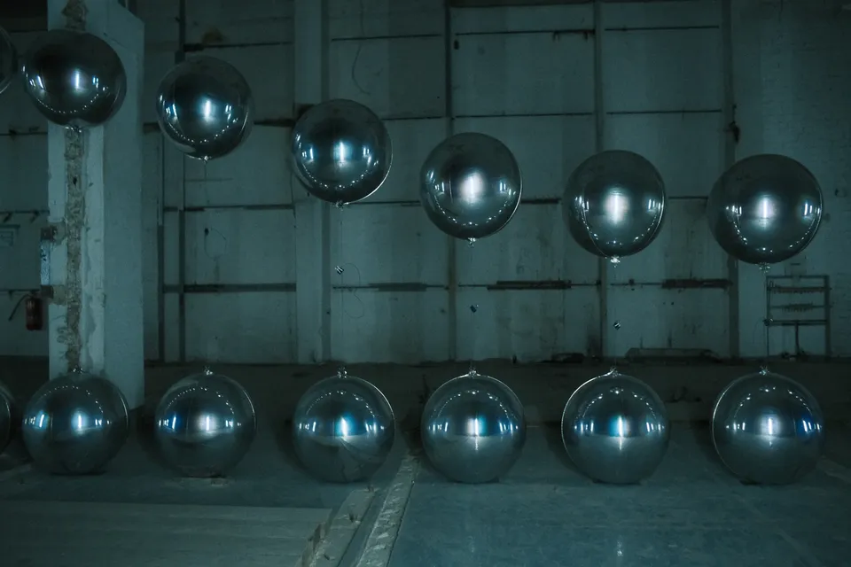 Zwei Reihen glänzender, reflektierender Metallkugeln in einem industriell anmutenden Raum.