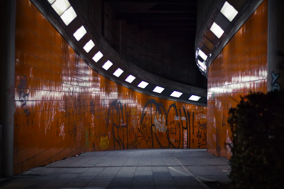 Eine gebogene, orangefarbene Wand mit Graffiti unter einer Reihe von quadratischen Fenstern.
