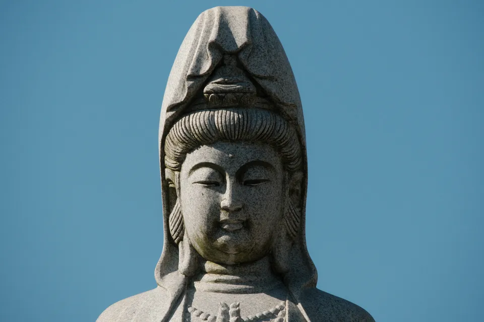Eine detailreiche Steinfigur mit geschlossenen Augen vor einem klaren blauen Himmel.