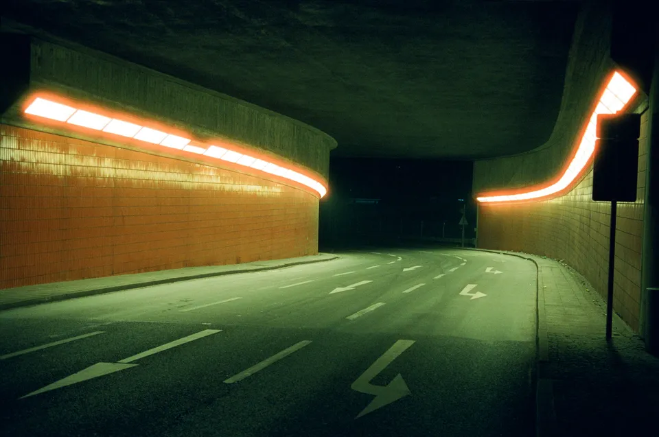 Eine Kurve in einem Tunnel mit leuchtenden orangefarbenen Lichtstreifen an den Wänden.