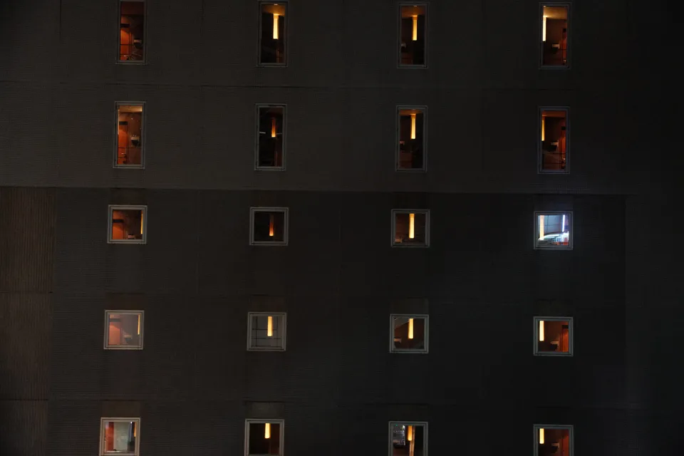 Eine Fassade mit mehreren Reihen von beleuchteten Fenstern in einer dunklen Nacht.